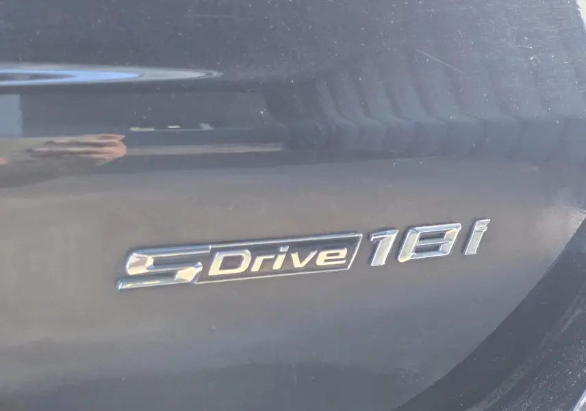 Gros plan sur l'emblème sDrive18i argenté sur la carrosserie noir saphir métallisé d'un BMW X1 F48.