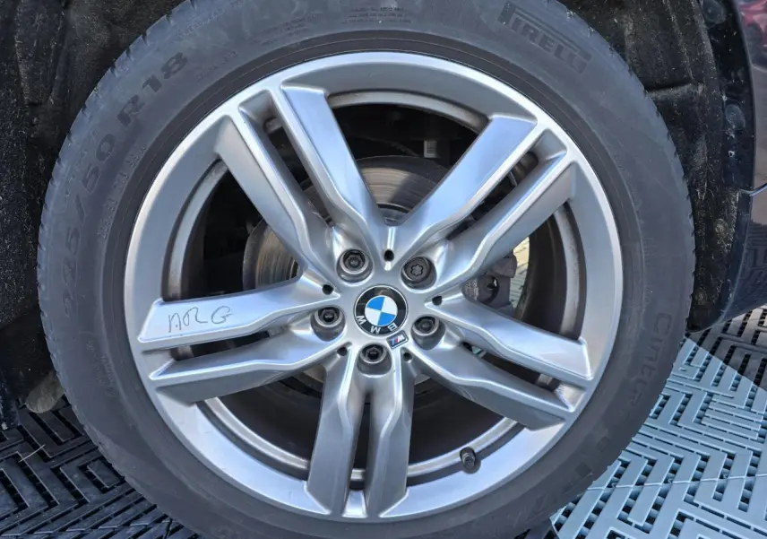 Gros plan sur la jante alliage 18 pouces bicolore M Sport d'un BMW X1 noir Saphir Metal, avec logo BMW central.