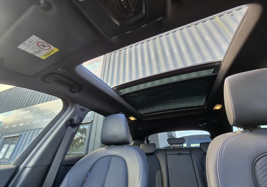 Vue intérieure du toit ouvrant panoramique et des sièges avant en tissu noir du BMW X1 F48 noir saphir métal.