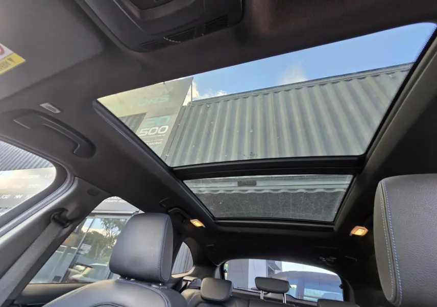 Toit ouvrant panoramique vu de l'intérieur arrière du BMW X1 noir Saphir Metal avec sièges en tissu noir et surpiqûres bleues