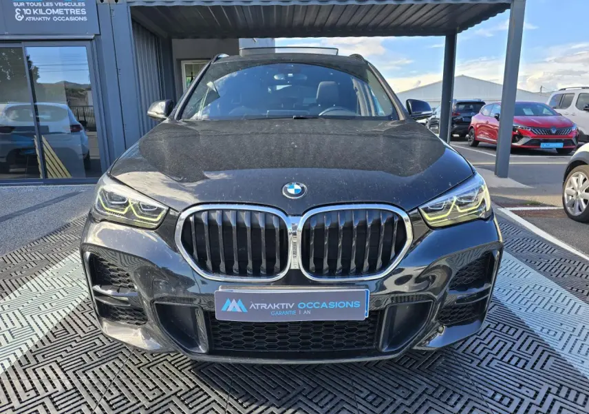 Vue frontale d'un BMW X1 noir saphir métallisé avec calandre double haricot et phares LED allumés.