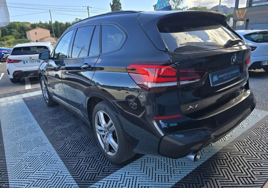 BMW X1 noir saphir métal vue 3/4 arrière droit, avec sortie d'échappement chromée et vitres teintées.