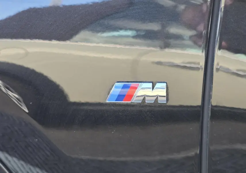 Gros plan sur l'emblème M tricolore sur la porte latérale gauche d'un BMW X1 noir saphir métallisé.
