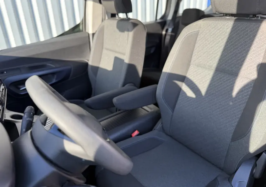 Vue intérieure rapprochée des sièges avant en tissu gris du Peugeot Rifter 1.5 BlueHDi 130, avec accoudoirs et volant partiel.