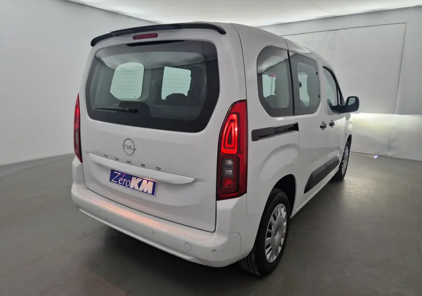 Vue 3/4 arrière droite d'un Opel Combo Life blanc avec feux arrière allumés et becquet noir sur toit.