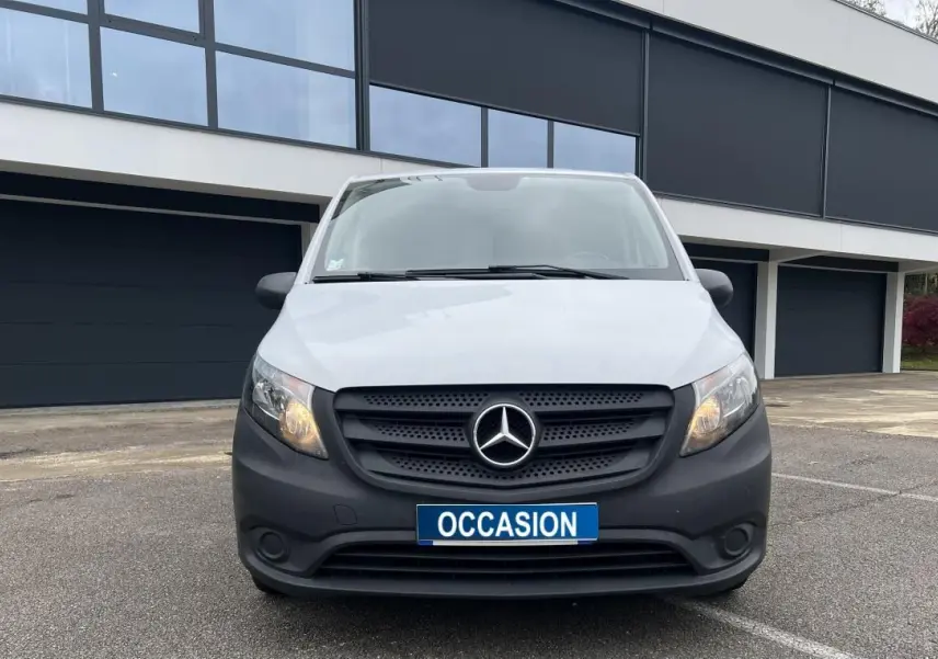 Vue frontale d’un Mercedes Vito Fourgon blanc avec calandre noire et plaque « OCCASION » en extérieur devant un bâtiment moderne.