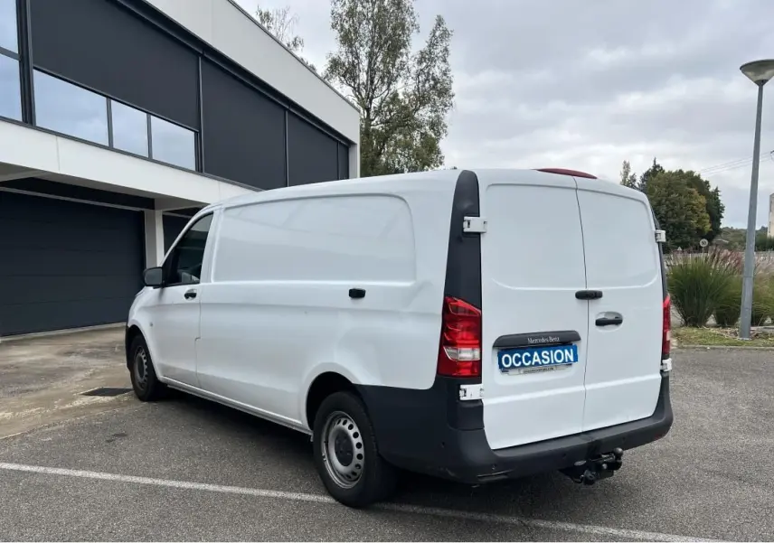 Vue 3/4 arrière droite d’un Mercedes Vito Fourgon blanc avec attelage et porte latérale, stationné en extérieur.