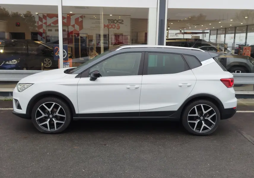 Vue de profil côté gauche d'un SEAT Arona blanc avec toit gris magnétique et jantes alliage noires et argentées.