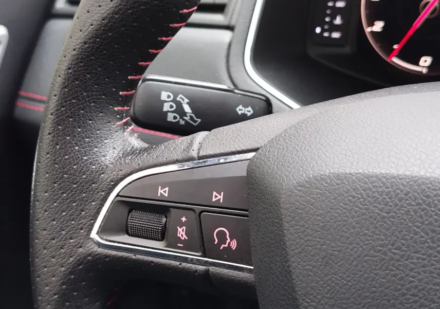 Gros plan sur les commandes multimédia à gauche du volant en cuir noir avec surpiqûres rouges du SEAT Arona 2020.