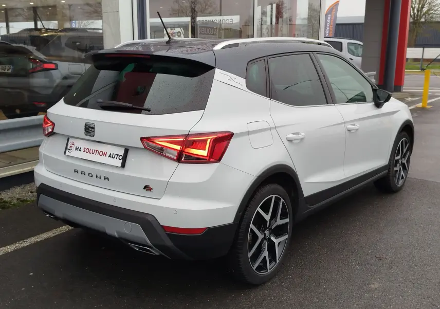 Vue 3/4 arrière droite d'un SEAT Arona blanc avec toit gris magnétique, feux arrière allumés et jantes alliage noires.