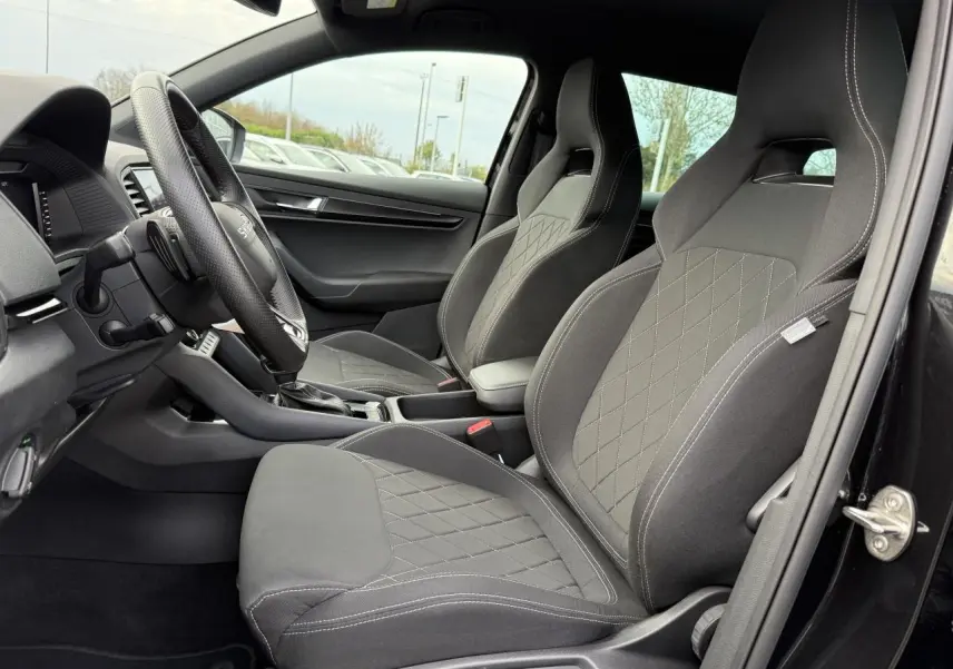 Vue intérieure côté conducteur du Skoda Karoq noir Magic nacré, mettant en valeur les sièges sport en tissu noir avec surpiqûres contrastées.