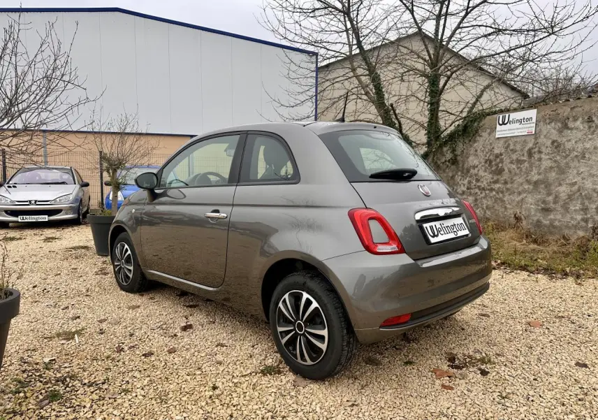 Fiat 500 gris foncé vue 3/4 arrière droit, jantes alliage et poignées chromées visibles.