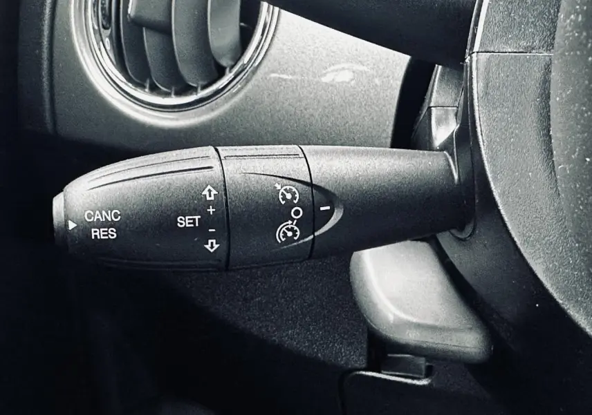 Gros plan sur la commande de régulateur de vitesse à gauche du volant dans l'habitacle gris foncé d'une Fiat 500 2023.