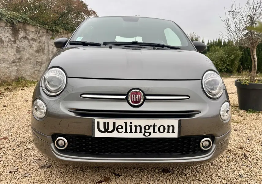 Vue avant rapprochée d'une Fiat 500 gris foncé 2023 avec projecteurs ronds et calandre chromée.