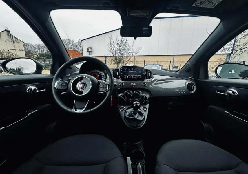 Vue intérieure frontale du tableau de bord gris foncé et volant noir de la Fiat 500 2023 avec boîte manuelle.