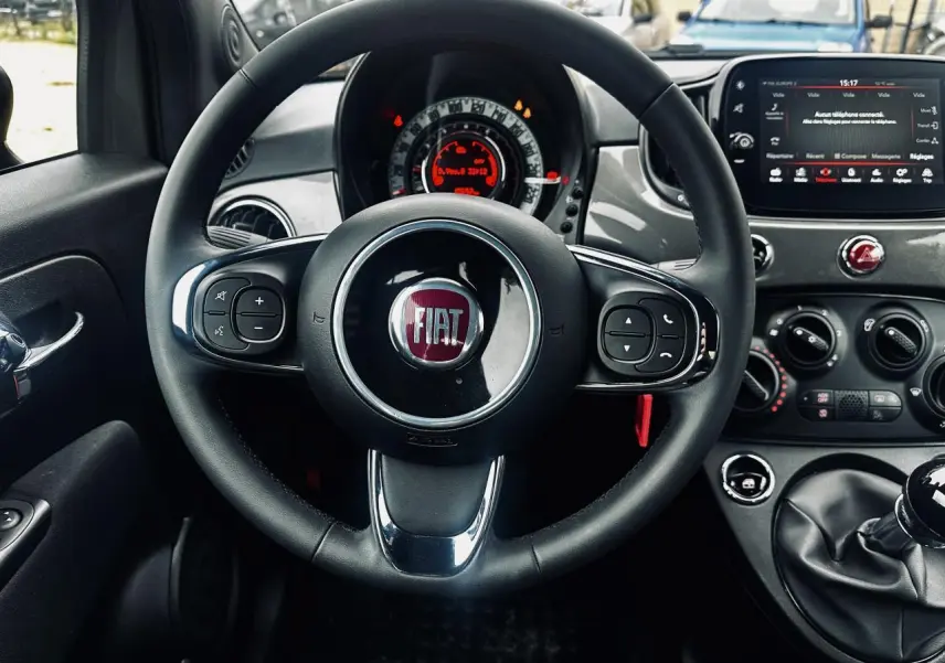 Vue intérieure centrée sur le volant noir en éco-cuir de la Fiat 500 gris foncé avec tableau de bord et écran tactile.