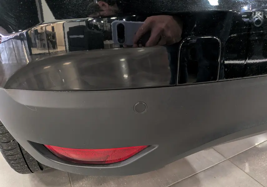 Gros plan sur le pare-chocs arrière noir étoilé du Renault Scénic IV, avec feu antibrouillard et capteur de recul visible.