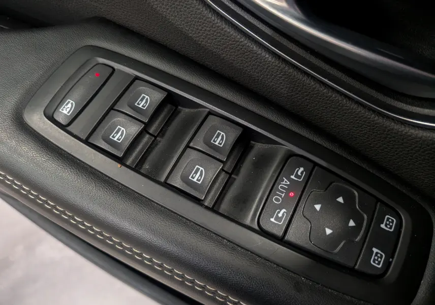 Gros plan sur les commandes de lève-vitres et rétroviseurs électriques sur la porte côté conducteur en cuir noir du Renault Scénic IV.