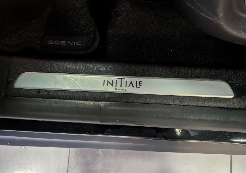 Gros plan sur la plaque de seuil de porte "Initiale Paris" et tapis noir du Renault Scénic IV noir étoilé.