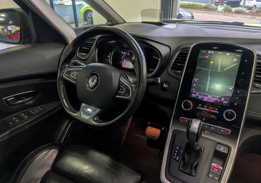 Vue intérieure côté conducteur du Renault Scénic IV noir étoilé, avec volant cuir, écran tactile central et levier de boîte automatique.
