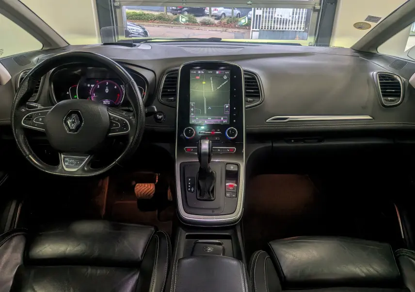 Vue intérieure avant du Renault Scénic IV noir étoilé, mettant en valeur le volant multifonction, l'écran tactile central et la console avec boîte automatique.