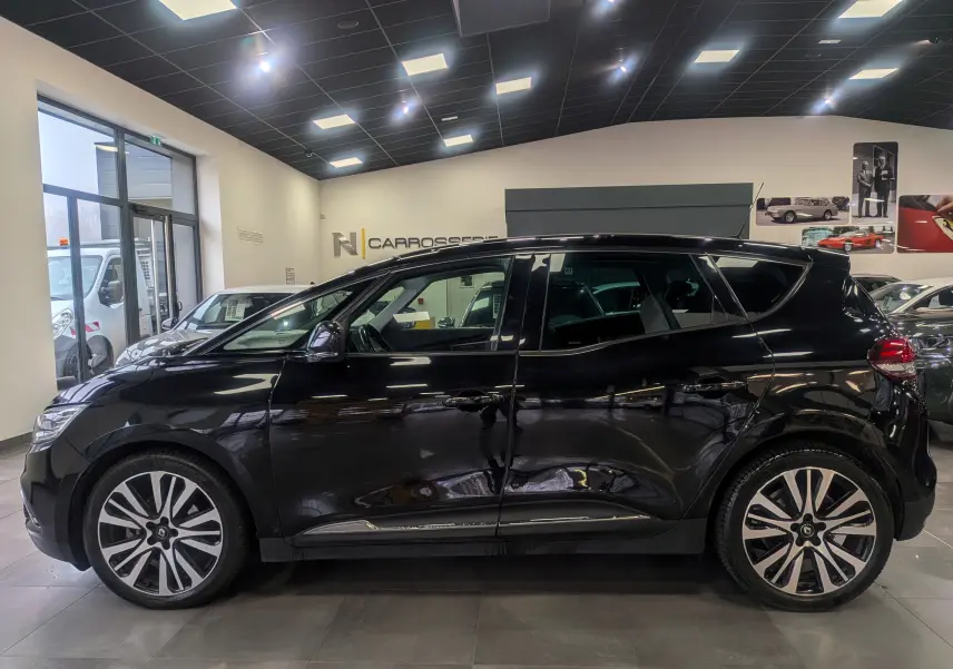 Profil gauche d’un Renault Scénic IV noir étoilé en showroom, soulignant ses jantes bi-ton et lignes fluides.