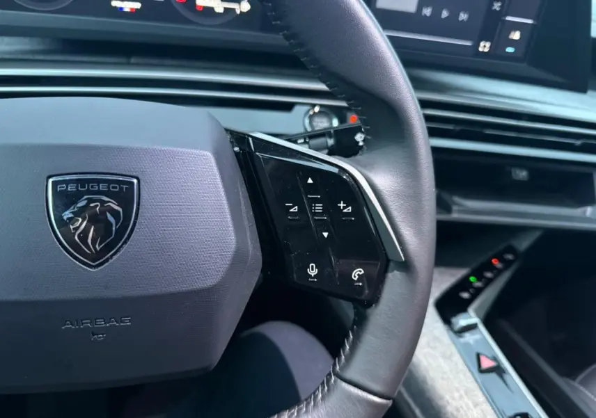 Gros plan sur le volant cuir noir du Peugeot 3008 Hybrid 145 e-DCS6 Allure 2025 avec commandes intégrées et tableau de bord numérique.