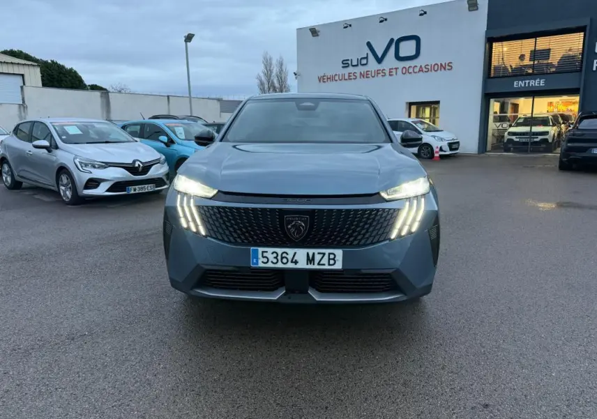 Vue frontale du Peugeot 3008 Hybrid bleu avec feux allumés et calandre distinctive sur parking de concession.