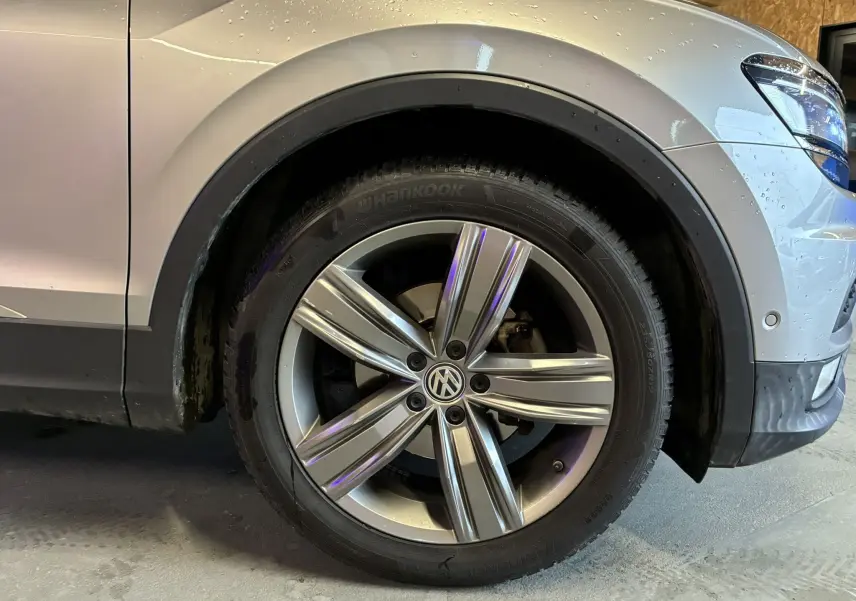 Gros plan sur la roue avant droite d’un Volkswagen Tiguan gris 2017 avec jante alliage 5 branches et logo VW central.