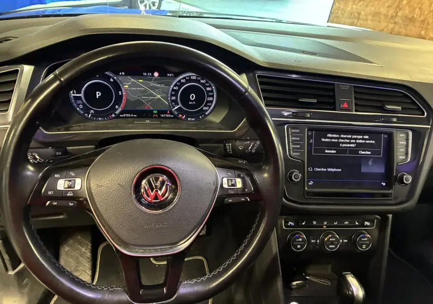 Vue intérieure du tableau de bord et volant noir du Volkswagen Tiguan 2.0 TDI 150 Carat avec écran central et commandes au volant.