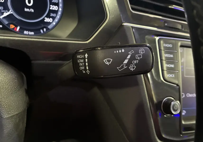 Gros plan sur la commande d’essuie-glace du Volkswagen Tiguan 2.0 TDI 150 Carat, intérieur noir avec tableau de bord numérique.