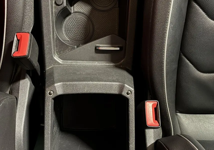 Vue plongeante sur la console centrale noire en cuir du Volkswagen Tiguan 2.0 TDI 150 Carat avec porte-gobelets et ceintures rouges.