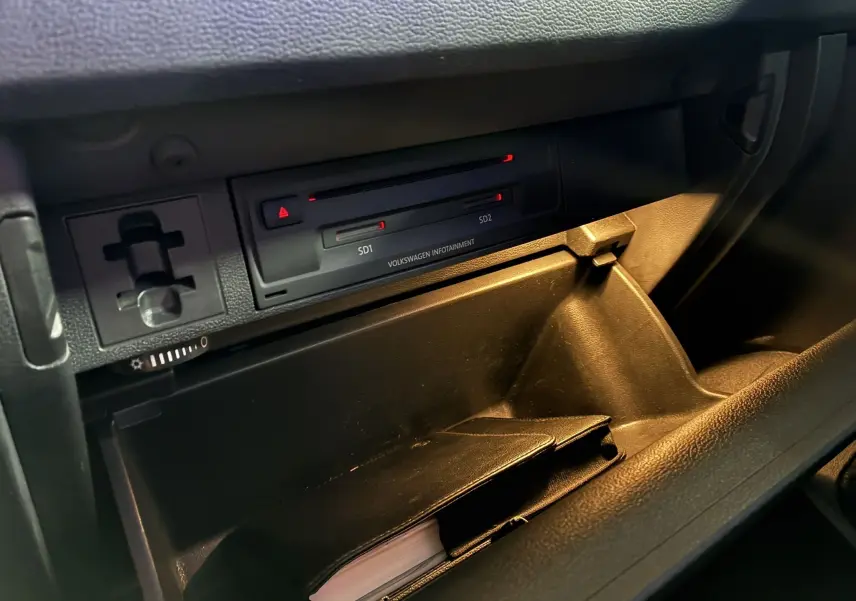 Gros plan sur la boîte à gants ouverte du Volkswagen Tiguan gris 2017, montrant le lecteur SD et un carnet noir à l'intérieur.