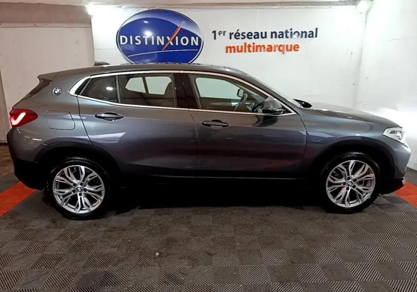 BMW X2 sDrive18i Lounge gris foncé vue de profil côté gauche, avec jantes alliage et feux arrière allumés.