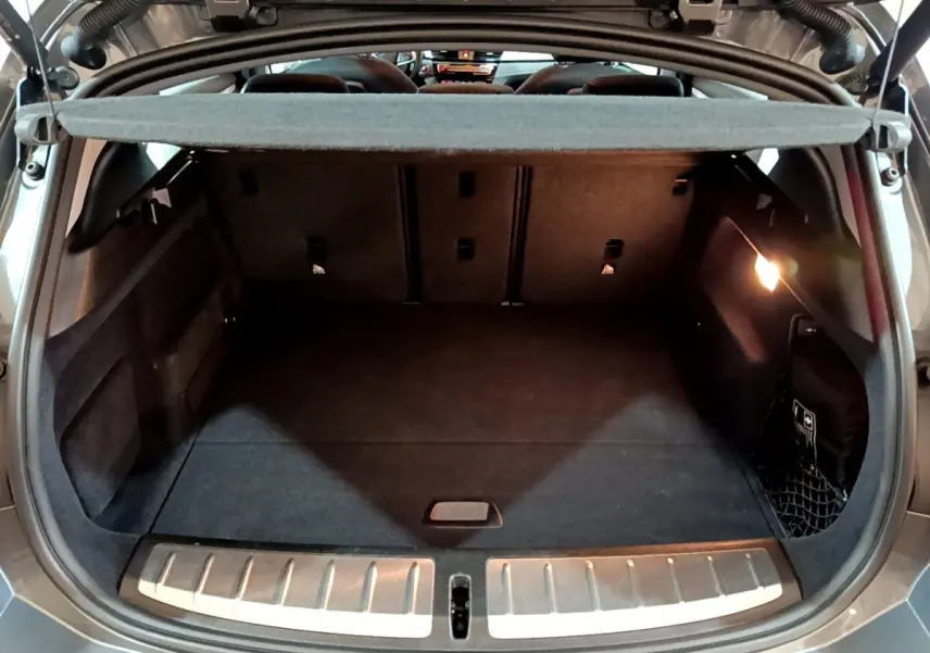 Coffre ouvert vu de l'arrière d'une BMW X2 gris foncé, avec tapis noir et éclairage intérieur à droite.