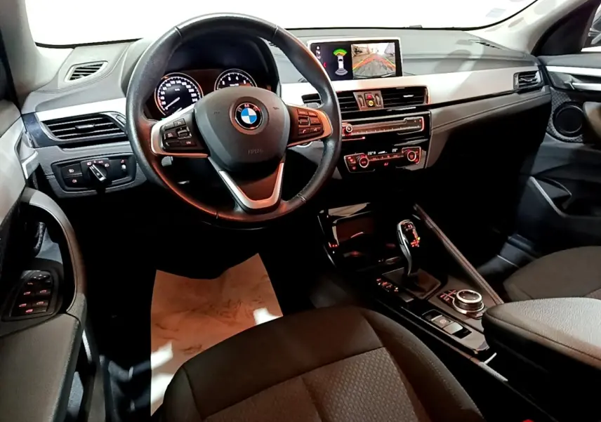 Vue intérieure côté conducteur du tableau de bord et console centrale de la BMW X2 sDrive18i Lounge DKG7, avec écran multimédia allumé.