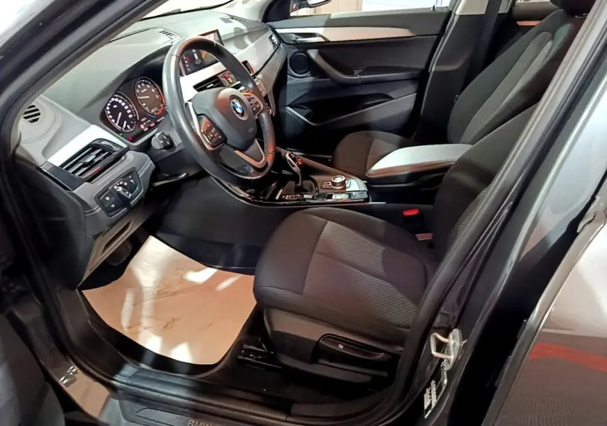 Vue intérieure côté conducteur du BMW X2 gris foncé, montrant le volant cuir multifonctions et la console centrale.