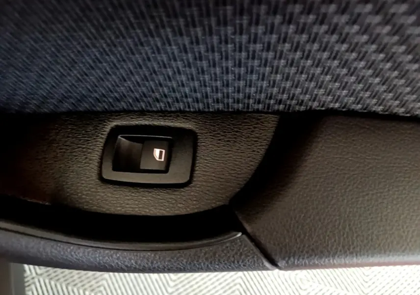 Détail du bouton de commande de lève-vitre sur la porte intérieure d’un BMW X2 gris foncé.