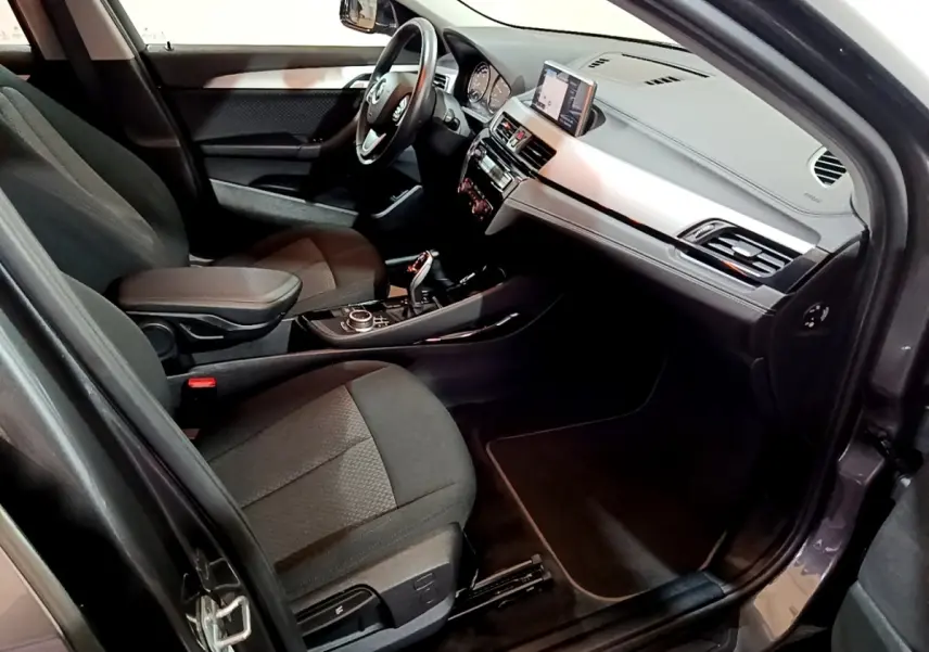 Vue intérieure côté conducteur de la BMW X2 sDrive18i Lounge 2021, avec tableau de bord moderne et sièges gris foncé.