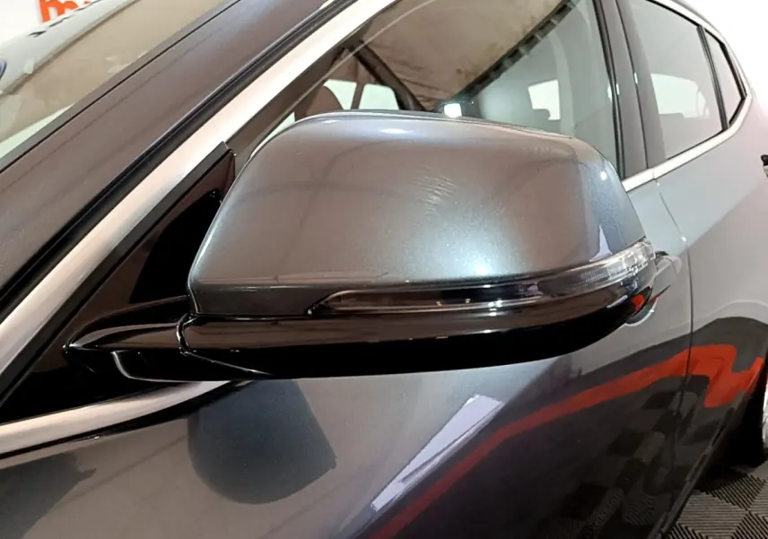 Gros plan sur le rétroviseur droit gris foncé d'une BMW X2 sDrive18i Lounge DKG7, avec la porte arrière visible en arrière-plan.