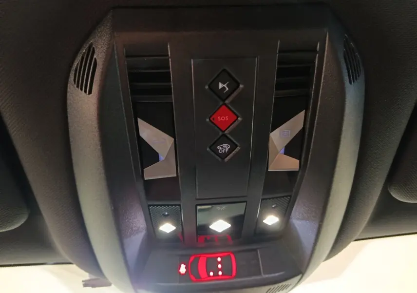 Vue en contre-plongée du panneau de commandes au plafond intérieur du DS7 Crossback noir, avec boutons SOS et éclairage LED allumé.