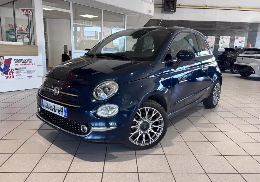Vue 3/4 avant d'une Fiat 500 bleu foncé avec jantes alliage et toit panoramique en showroom.