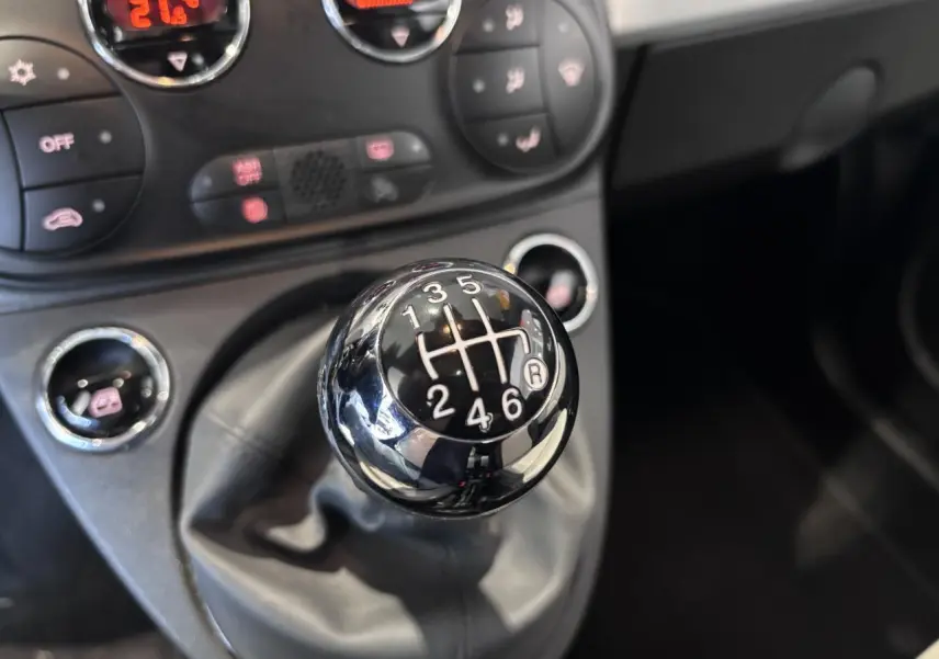 Gros plan sur le levier de vitesses manuel chromé de la Fiat 500 avec tableau de bord noir en arrière-plan.