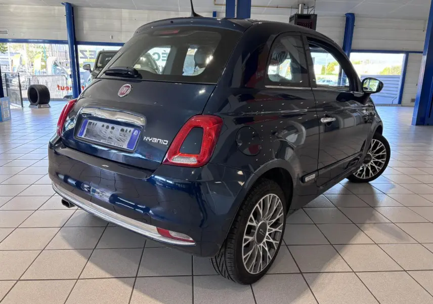 Vue 3/4 arrière droite d'une Fiat 500 hybride bleu foncé avec jantes alliage et détails chromés en showroom.