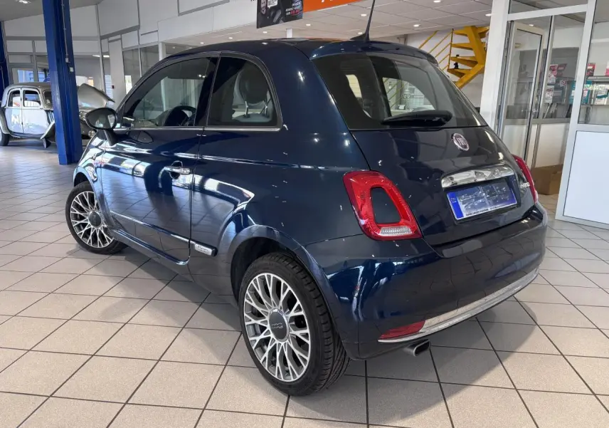 Fiat 500 bleu foncé vue 3/4 arrière droit en intérieur avec jantes alliage et détails chromés.