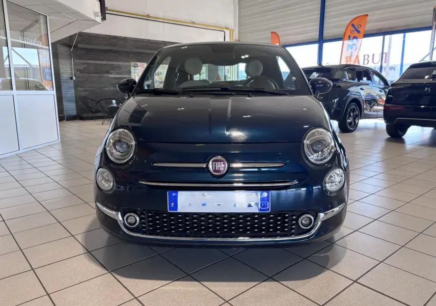Vue avant d'une Fiat 500 noire en showroom, mettant en valeur sa calandre chromée et ses phares ronds distinctifs.