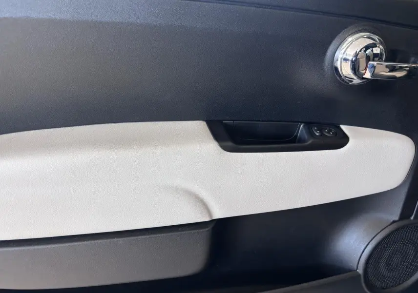 Gros plan sur la porte intérieure côté gauche de la Fiat 500 verte, avec poignée chromée et panneau bicolore noir et beige.