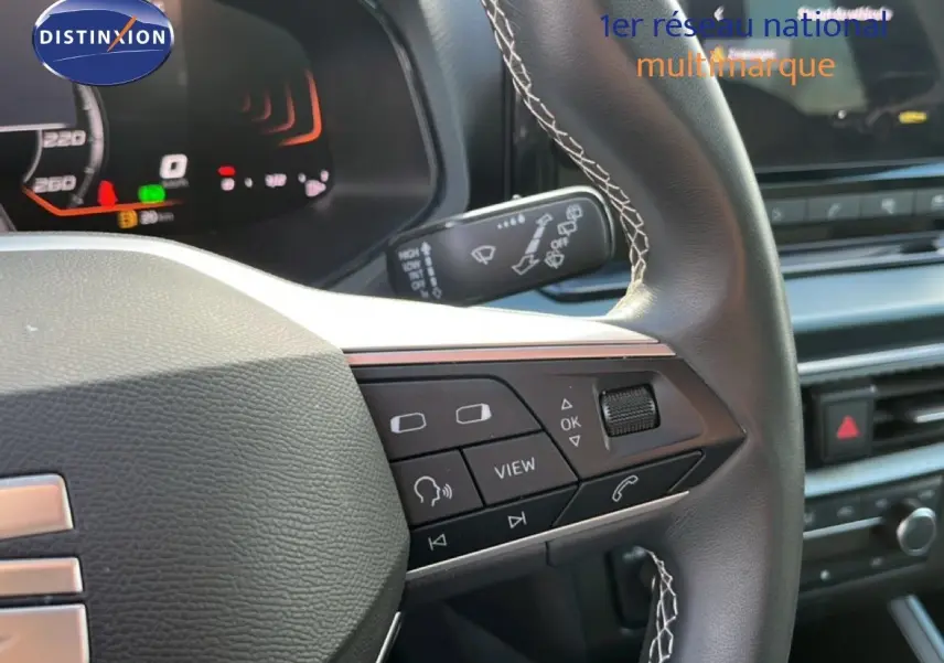 Gros plan sur le volant cuir noir à surpiqûres blanches du SEAT Arona 2025 avec commandes multifonctions et tableau de bord numérique.