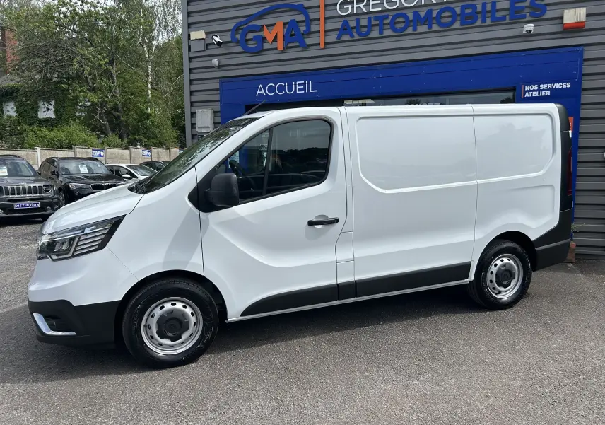 Renault Trafic Fourgon blanc en profil droit, stationné devant un bâtiment commercial avec logo GMA visible.