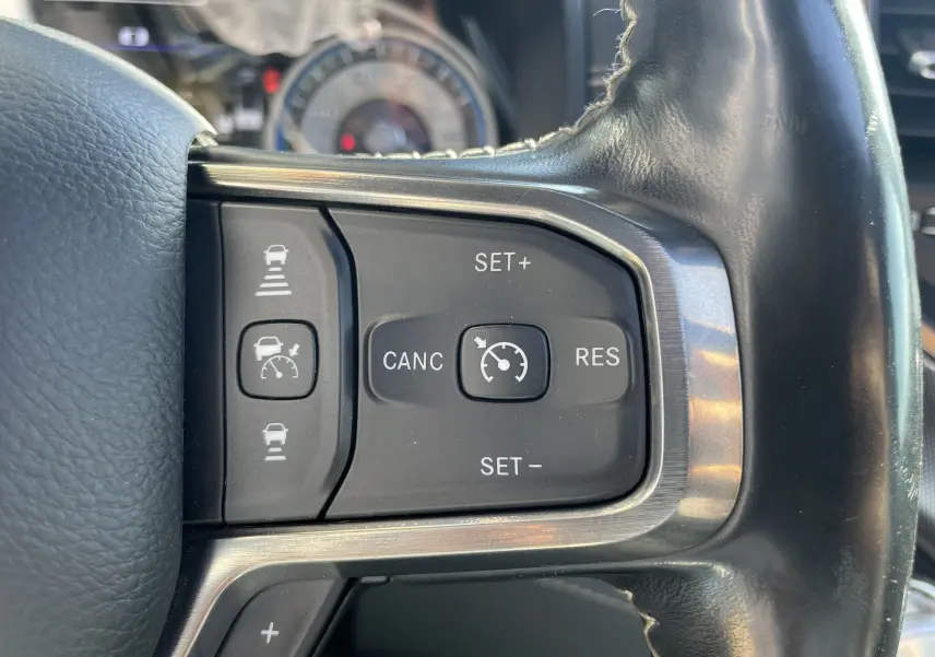 Gros plan sur les commandes de régulateur de vitesse au volant cuir noir du Dodge RAM 1500 blanc nacré.